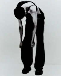 Model Enoch Cheung bending forward wearing black trousers against a stark white studio backdrop for Heliot Emil.
