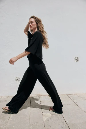 Model Jenn du Puy in a black outfit walking against a white textured wall by photographer Paolo Steve for Zara.