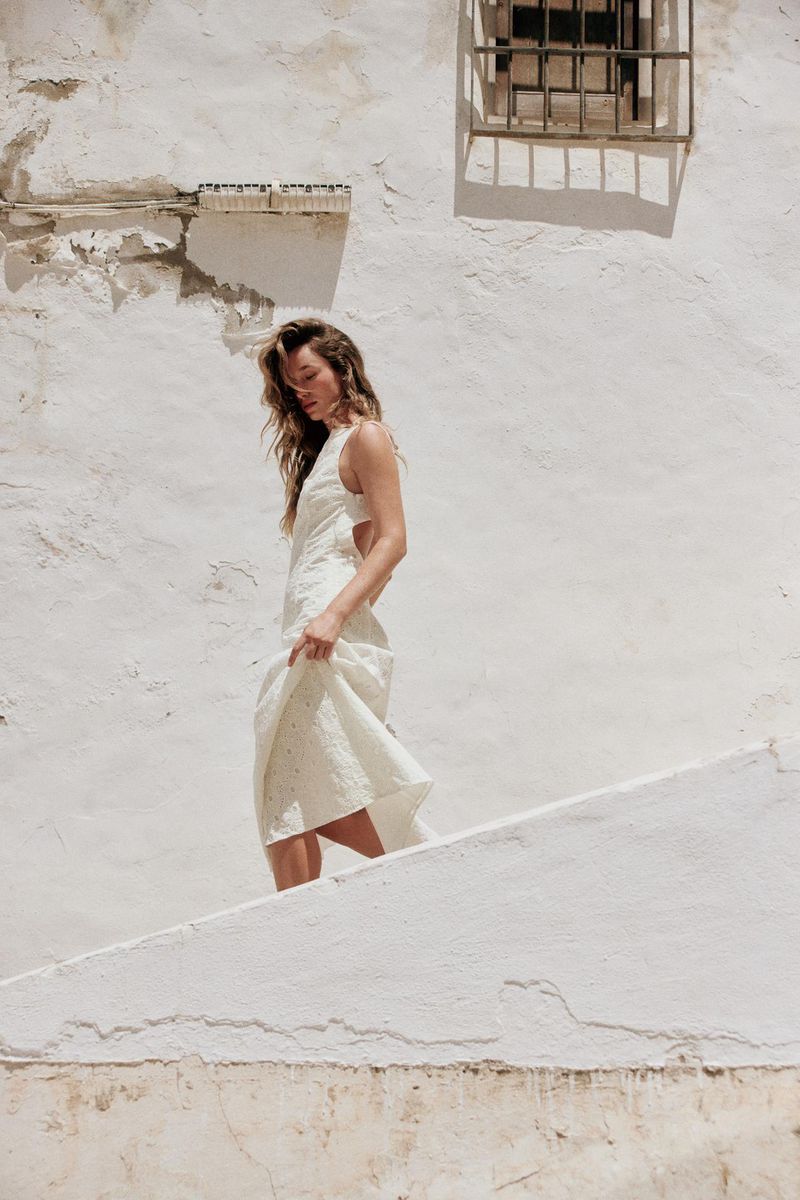 Model Jenn du Puy in a white dress walking down outdoor white stairs against a textured wall for Zara.
