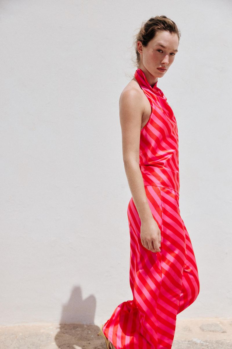 Model Jenn Du Puy in a pink and red striped outfit standing against a white wall for a Zara project.
