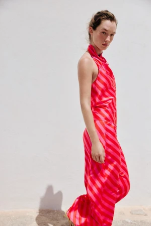 Model Jenn Du Puy in a pink and red striped outfit standing against a white wall for a Zara project.