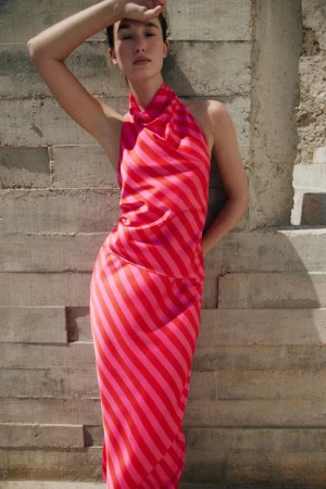 Model Jenn du Puy in a pink and red striped halter top and matching skirt leaning against a concrete wall.