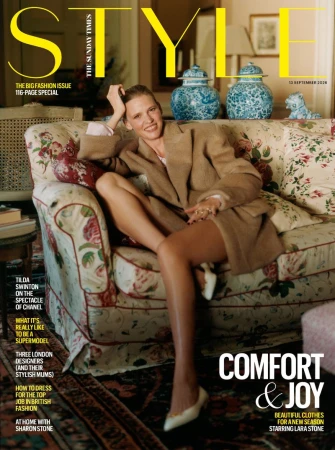 Model Lara Stone seated on a floral patterned sofa wearing a beige blazer and white heels for a magazine cover shoot