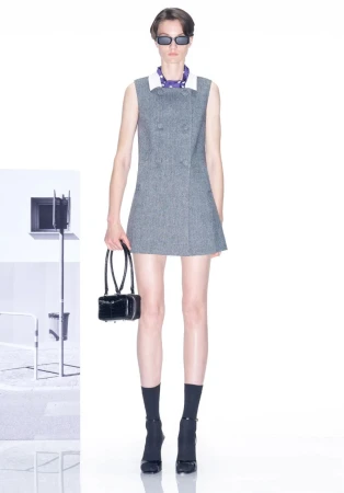 Fashion model wears grey mini dress with black accessories in bright studio. Studio lighting setup visible in soft focus background.