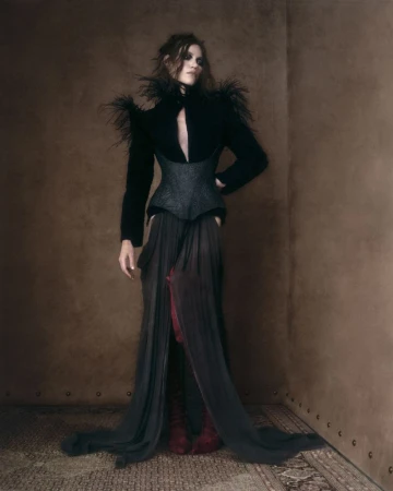 Model in black feathered top and flowing skirt posing against a textured brown studio corner by Virginia Kluiters
