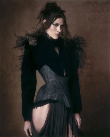 Model in dark feathered top and structured grey corset against a muted textured brown background by Virginia Kluiters
