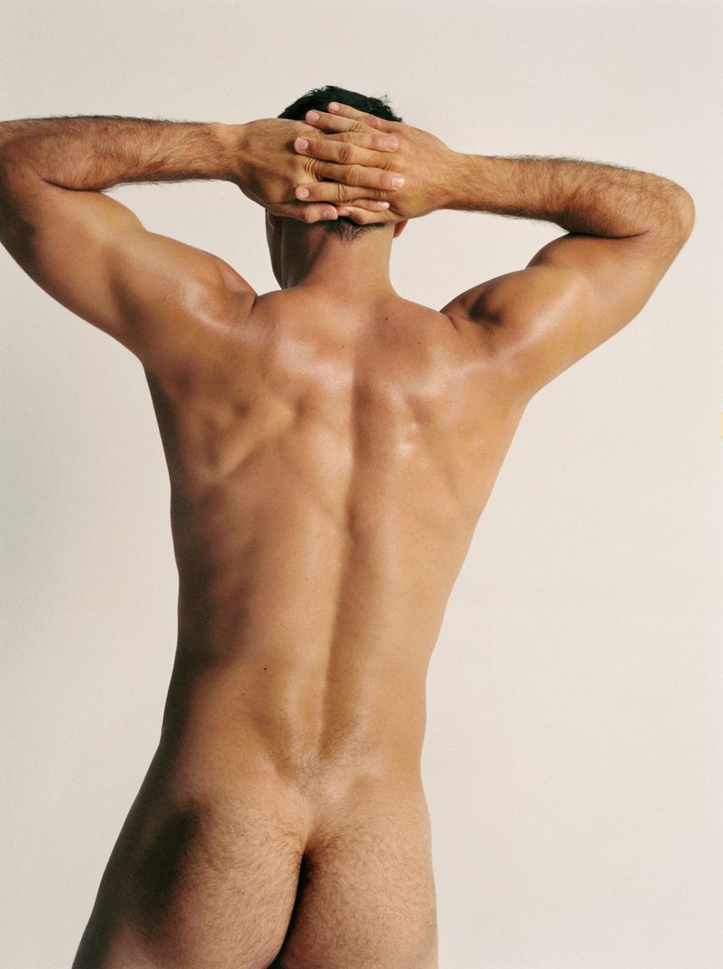 Rear view of a man with his hands clasped behind his head against a seamless white background