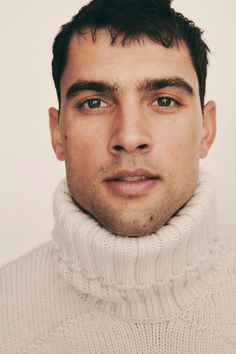 Close-up portrait of a man wearing a cream turtleneck sweater against a plain white background