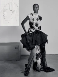 Black and white fashion portrait of a model wearing a lace dress and boots with a paper sketch pinned to the background.