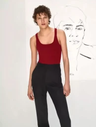 Model wearing a red tank top and black trousers standing against a plain white background with a sketch drawing