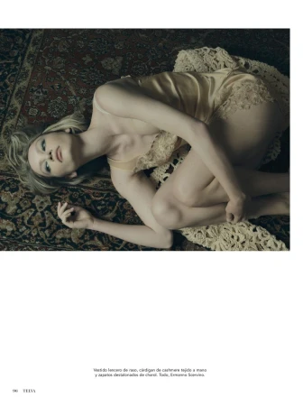Model Barbara Shilova lying on an ornate patterned rug wearing a satin slip dress and cashmere cardigan for Telva