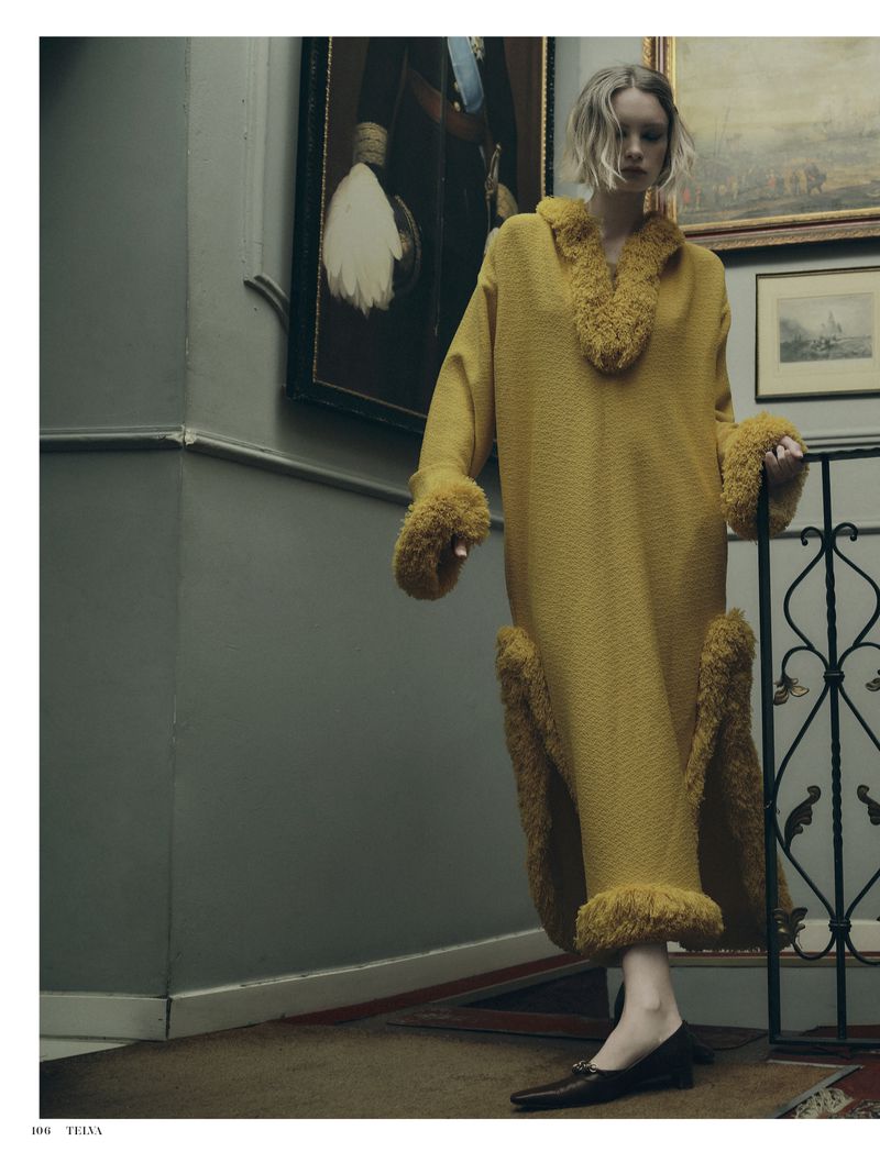 Model wearing a long yellow textured dress with faux fur trim on an indoor staircase