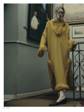 Model wearing a long yellow textured dress with faux fur trim on an indoor staircase