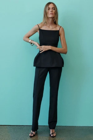 Model wearing a black camisole top and trousers standing against a turquoise background for A.L.C S/S 27