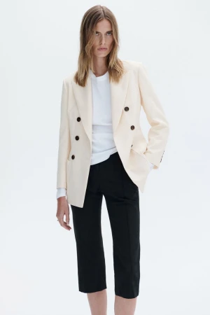 Model wearing a cream double-breasted blazer and black trousers against a white background for A.L.C S/S 27.