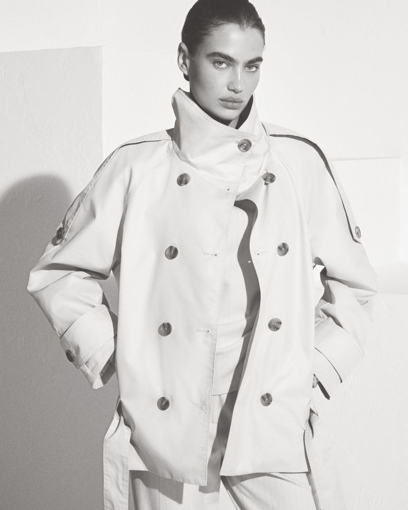 Model wearing a double-breasted collared coat against a plain white studio background