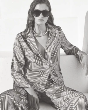Model in patterned shirt and trousers wearing dark sunglasses against a white background