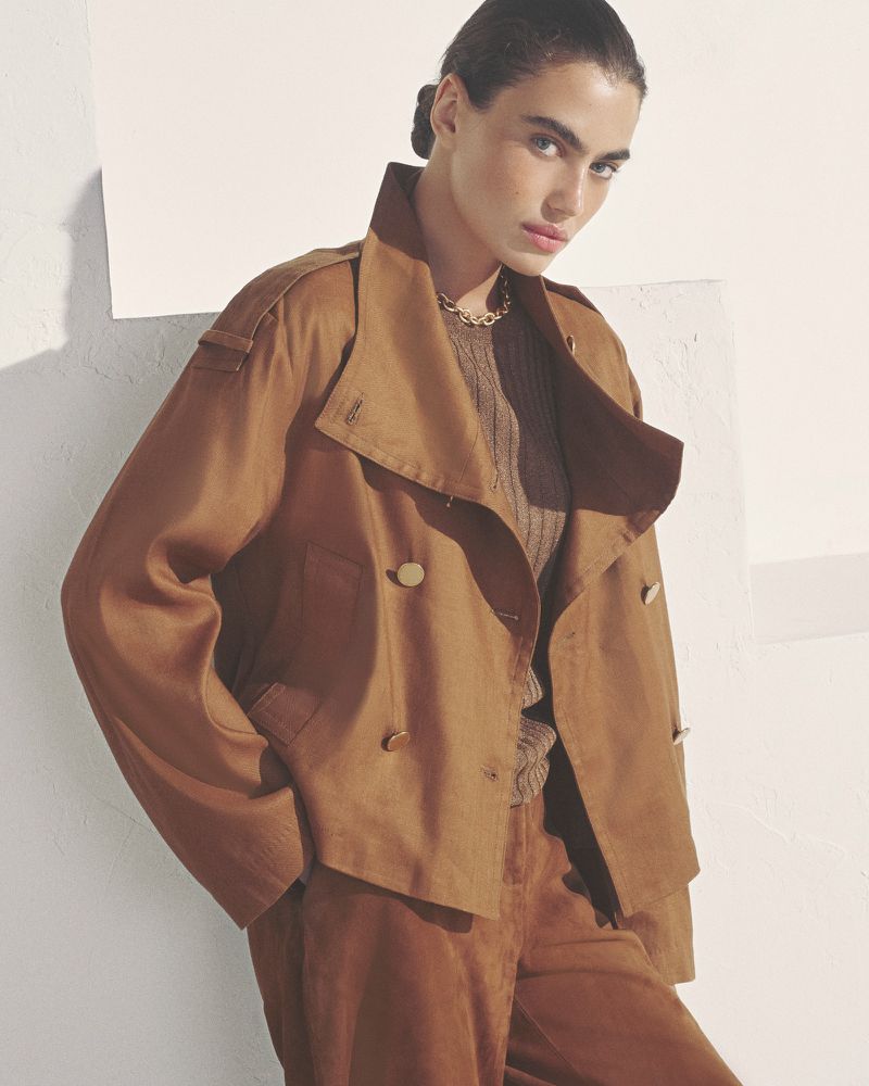 Model wearing a structured brown jacket and matching trousers against a light minimalist wall for Donna Karan SP27