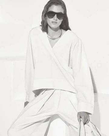 Model wearing dark sunglasses and a white V-neck top against a minimal white studio background.