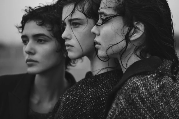 Three female models with wet textured dark hair wearing wool tweed coats in a black and white close-up profile portrait.