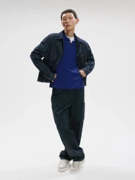 Model wearing a dark jacket, blue polo shirt, and dark trousers against a white seamless background