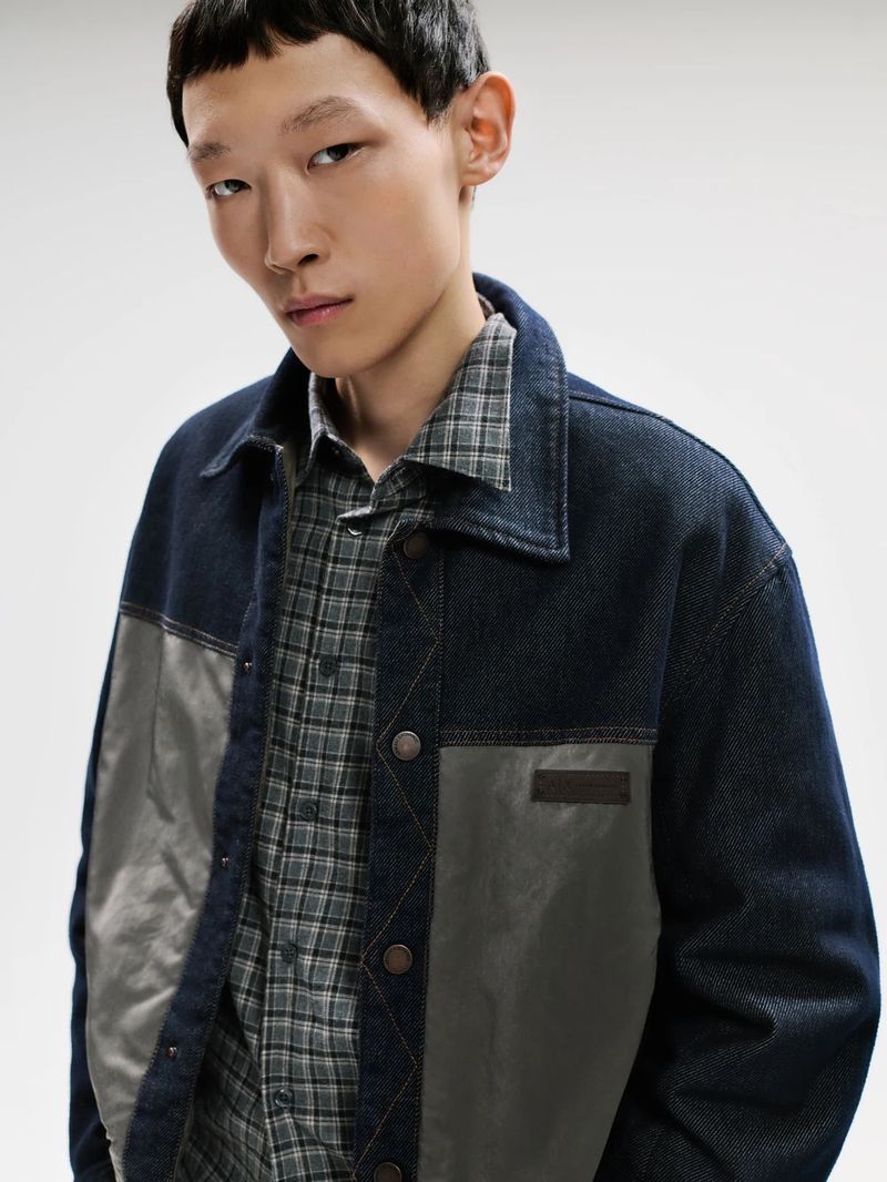 Model wearing a dark blue denim jacket and a grey plaid shirt against a clean plain white background.
