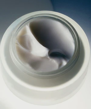 Top-down view of an open jar of skincare cream with smooth white and grey swirled textures set on a bright white surface.