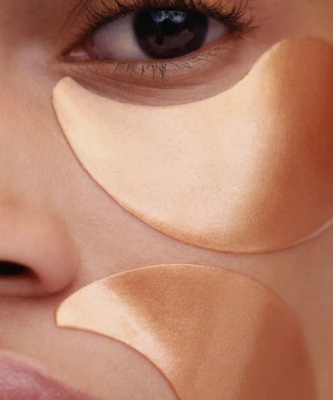 Close-up of a person's face wearing two golden under-eye patches for skincare, captured by photographer Alain Vasallo.