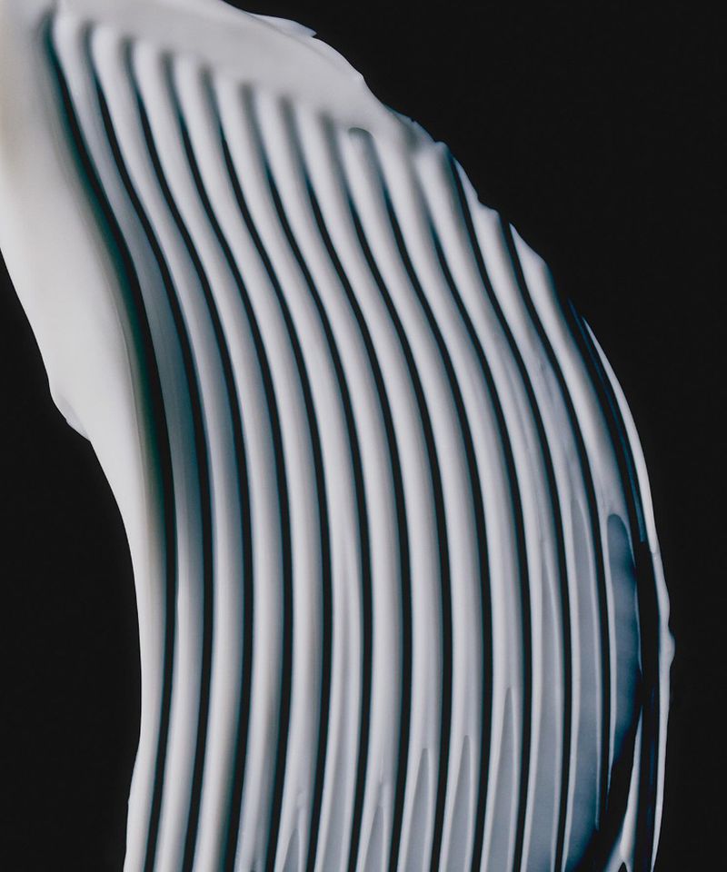 A curved white cream smear showing pronounced parallel ridges against a stark black background.