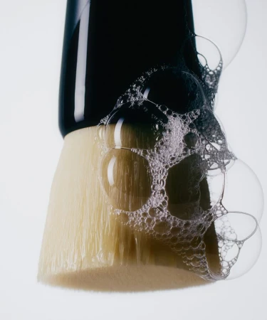 Close-up of a cosmetic makeup brush covered in soap bubbles against a clean white background