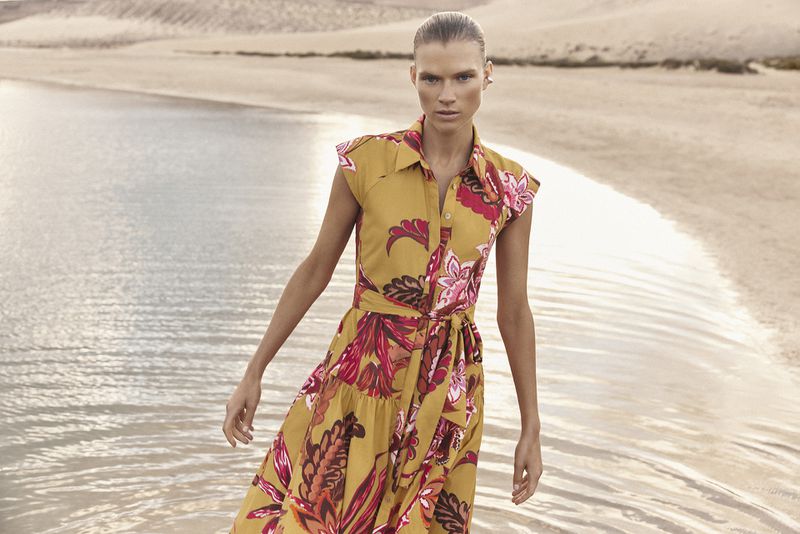 Model standing by water wearing a yellow floral print midi dress for Pedro del Hierro summer campaign.
