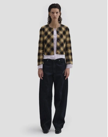 Full-length studio portrait of a model wearing a plaid cropped jacket, light shirt, and dark trousers against a white backdrop.