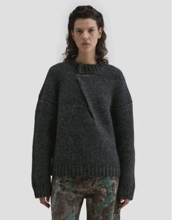 Model wearing a dark charcoal wool sweater with an asymmetric neckline against a plain light grey studio backdrop.