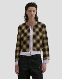 Model Romi Peled wearing a plaid jacket and dark trousers against a neutral background for Eckhaus Latta FW26.
