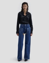 Model standing against a plain grey background wearing a black silk shirt and layered blue denim pants by Eckhaus Latta for FW26.