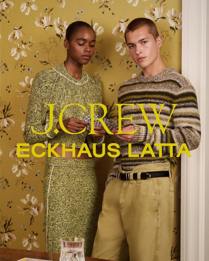 A Black woman and a white man posing together against an olive floral wallpaper background for a J.Crew and Eckhaus Latta campaign.