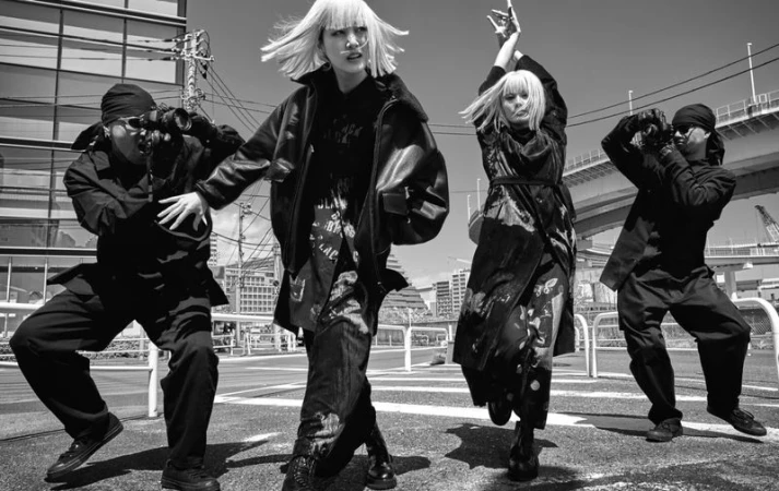 Monochrome urban fashion photography features two women with platinum wigs and two men with cameras in an outdoor setting.