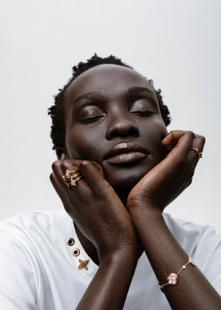 Close-up portrait of a Black woman with eyes closed, hands framing her face, wearing gold rings and a white top