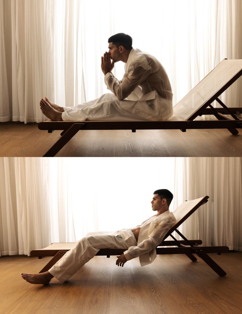Man in white attire resting on a wooden lounge chair against a window with white curtains in The Art of Becoming editorial.