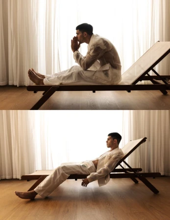 Man in white attire resting on a wooden lounge chair against a window with white curtains in The Art of Becoming editorial.