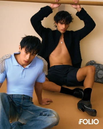 Two male models posing for Men's Folio Malaysia, one wearing a blue polo with fringe and denim jeans, the other in an open black jacket.