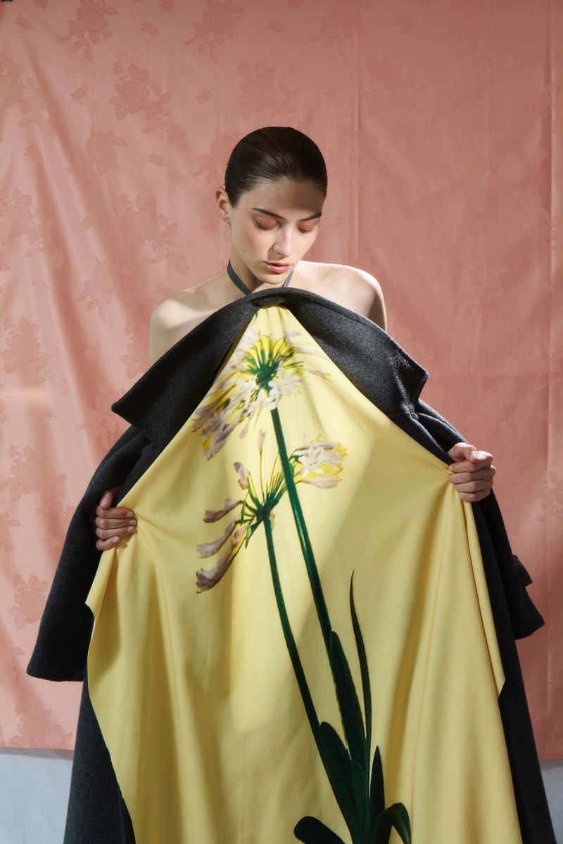 Model holding open a yellow floral coat against a textured pink backdrop for Flair Germany Florale Magie project.