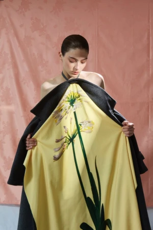 Model holding open a yellow floral coat against a textured pink backdrop for Flair Germany Florale Magie project.