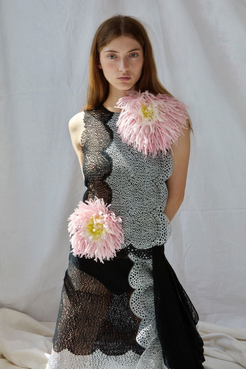 Model in black and white patterned dress with pink floral accents against white backdrop