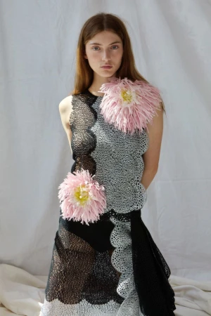 Model in black and white patterned dress with pink floral accents against white backdrop