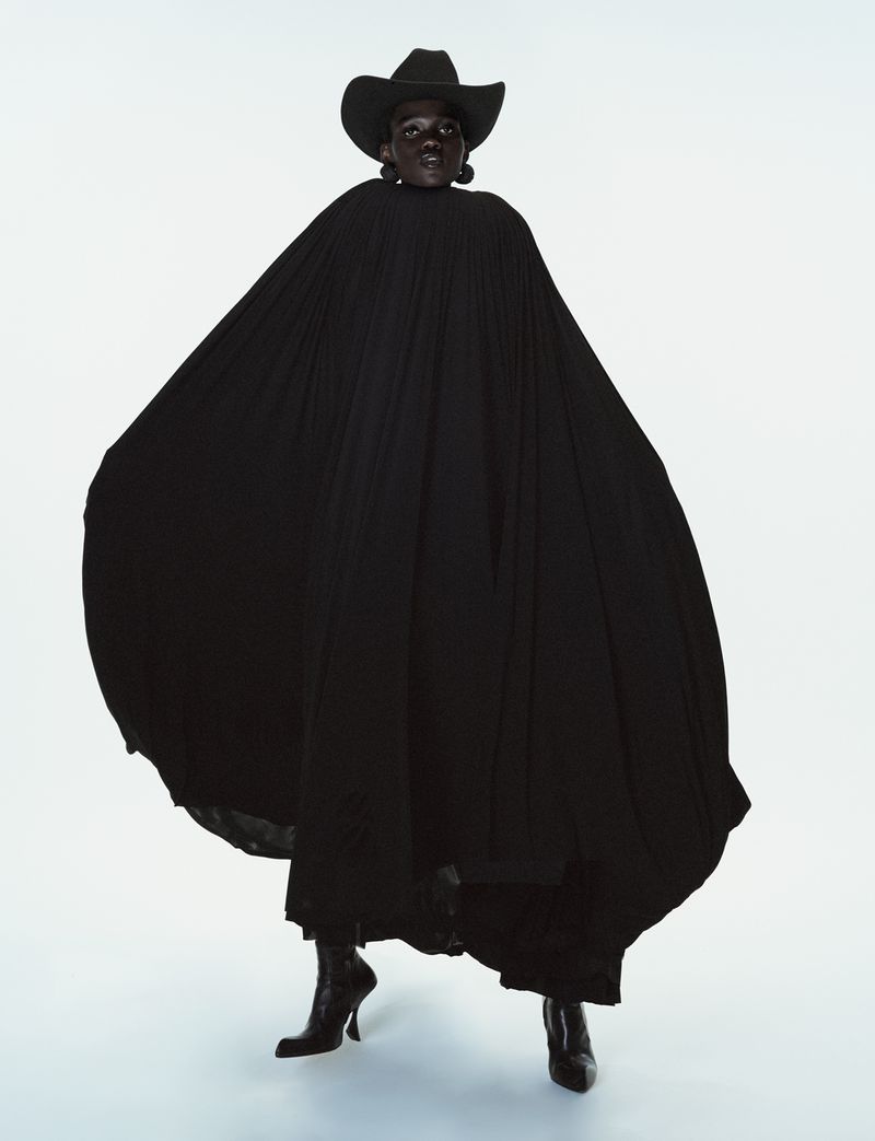 Caren Jepkemei wearing a large black pleated cape and cowboy hat against a white studio background for 10 Magazine