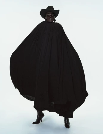 Caren Jepkemei wearing a large black pleated cape and cowboy hat against a white studio background for 10 Magazine