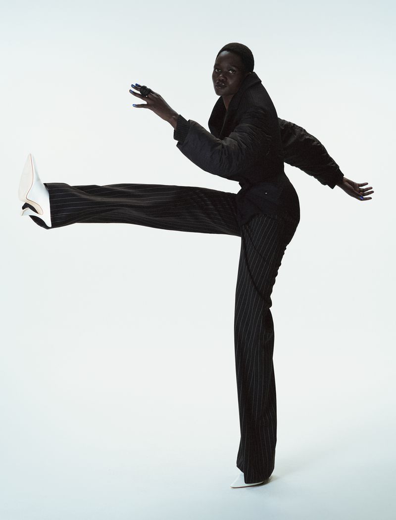 Model Caren Jepkemei captured mid-stride wearing a dark jacket and pinstripe trousers against a clean white background for 10 Magazine.