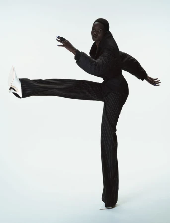 Model Caren Jepkemei captured mid-stride wearing a dark jacket and pinstripe trousers against a clean white background for 10 Magazine.