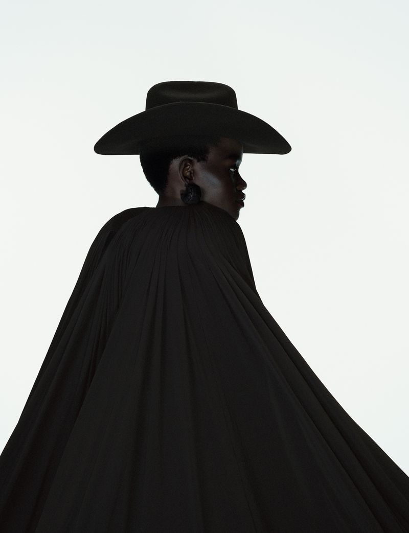 Model Caren Jepkemei wearing a black hat and pleated black cape against a white background for 10 Magazine